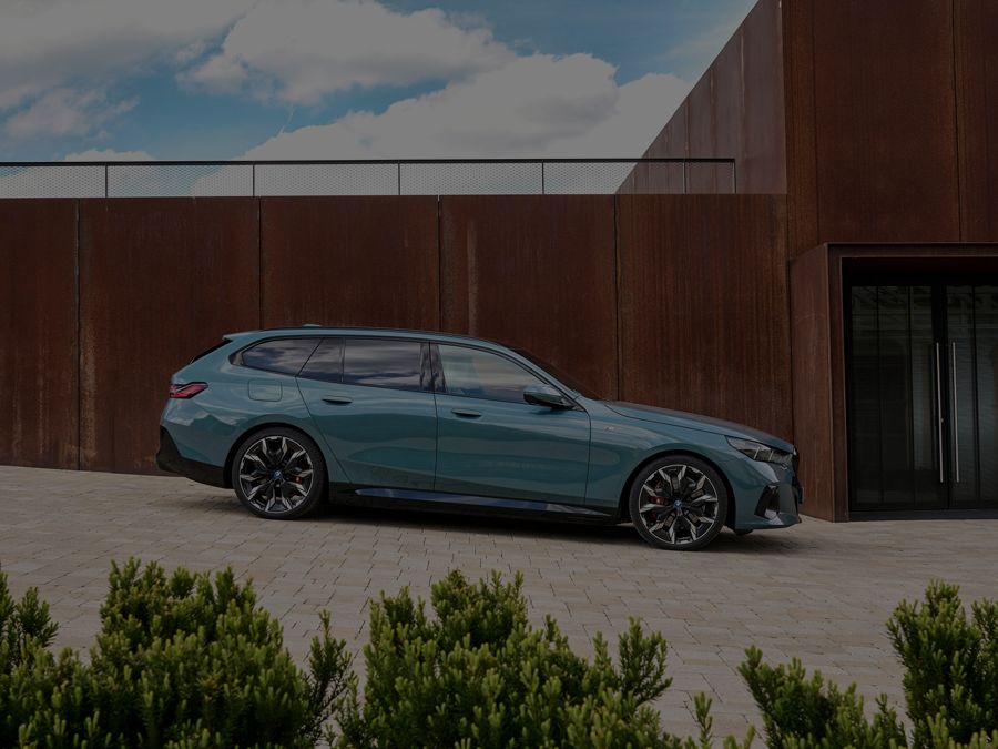 BMW i5 Touring parked by a building